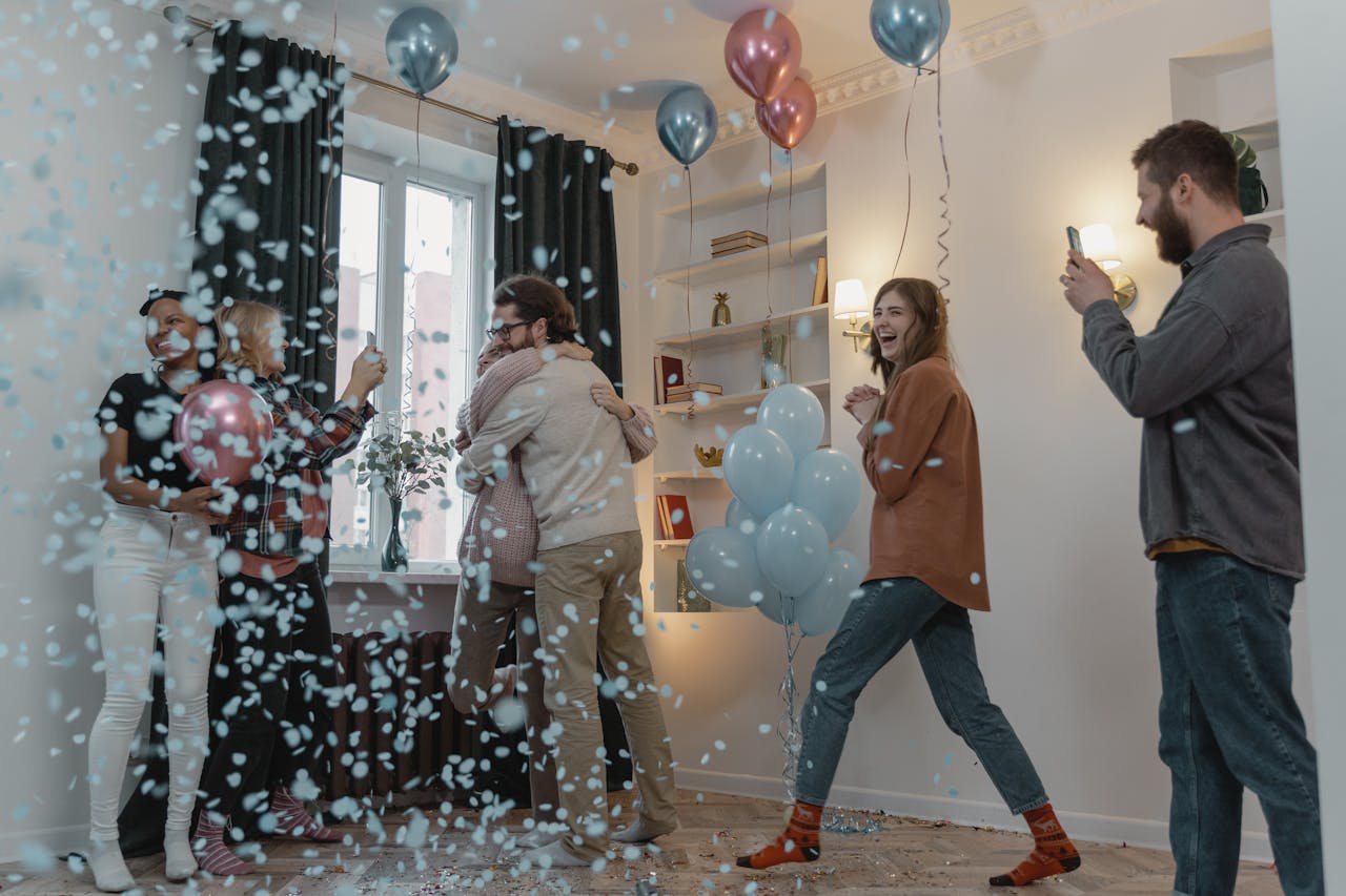 Group of friends celebrating a gender reveal with balloons and confetti indoors.