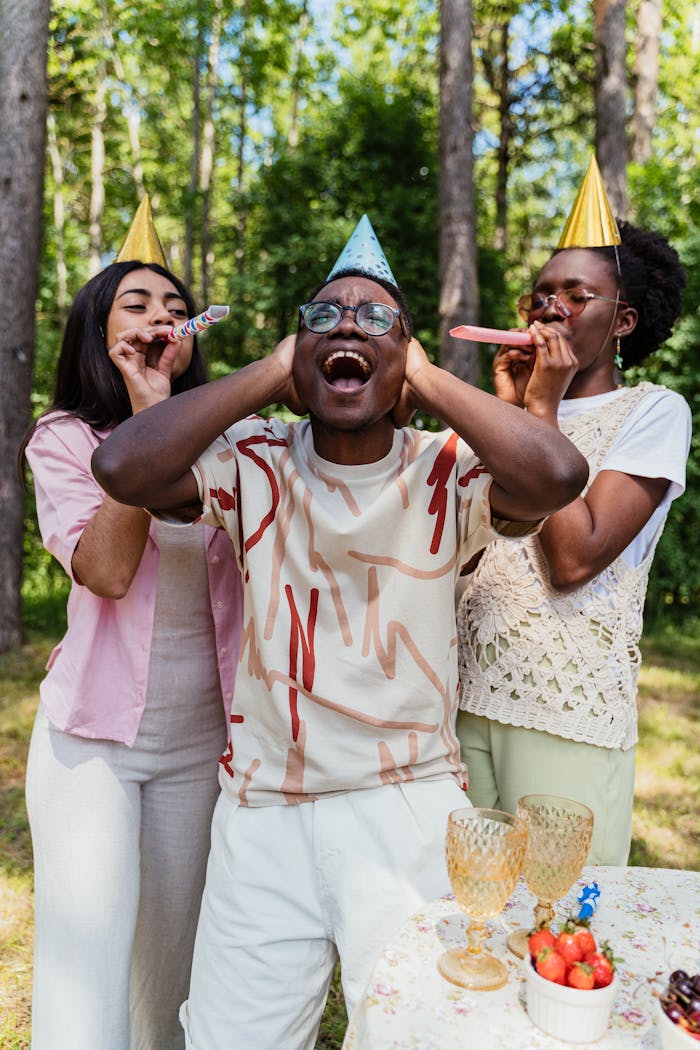 Group of friends celebrating a birthday outdoors with party hats and noisemakers.